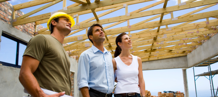Construction worker standing next to a man and woman looking up at the frame of a house. 